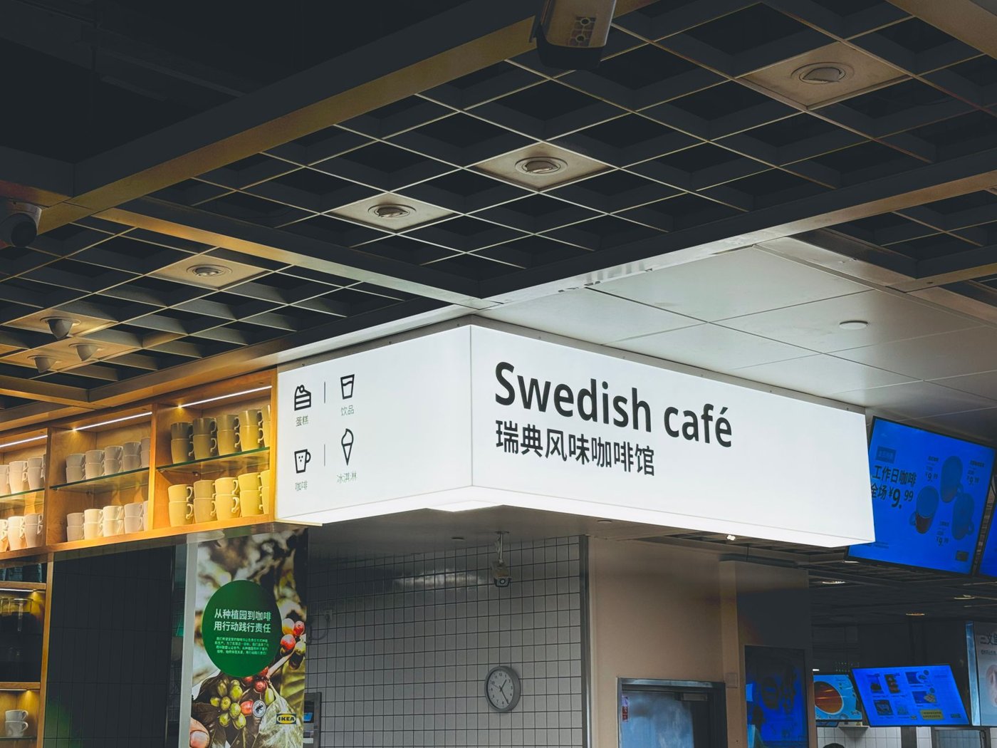 Beyaz ışıklı, üzerinde "Swedish café" yazan büyük bir tabela, kare ızgaralı koyu tavan altında asılı duruyor